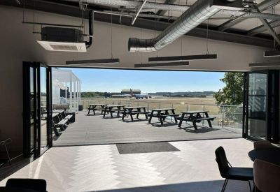Outdoor balcony terrace with picnic benches overlooking an active airfield.