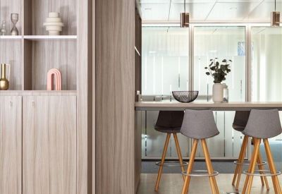 Modern office breakout area with light wood cabinets and grey bar stools.