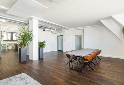 Open coworking space with dark wood floors, large potted plants, and a communal table.