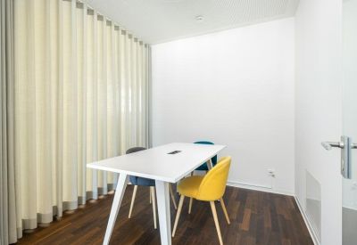 Small meeting room with a white table, yellow chairs, and floor-to-ceiling curtains.