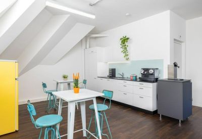 Bright breakroom kitchen with white cabinetry and teal seating under a sloped ceiling.