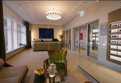 Reception area with a textured desk, modern chandelier, and emerald green velvet armchair.