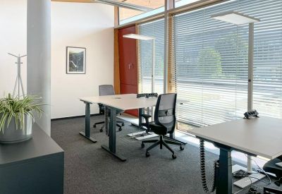 Bright private office suite with height-adjustable desks and ergonomic chairs near large windows.