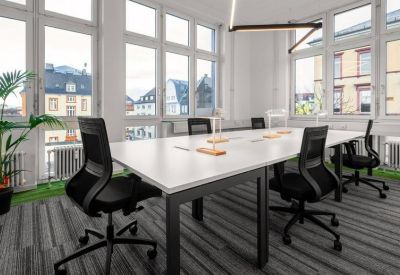 Sunny meeting room with a large white table, black mesh chairs, and floor-to-ceiling windows.