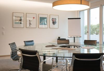 Modern conference room with a glass table, black leather chairs, and minimalist wall art.
