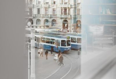 Outdoor courtyard view through a window showing a tram passing historic city buildings.