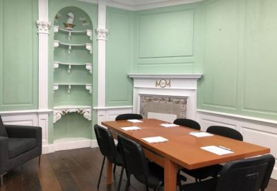 Meeting room with green walls and a wooden table for six.