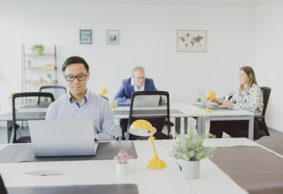 Open-plan office with professionals working at white desks with yellow task lamps.