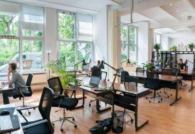 Open-plan office with multiple workstations, ergonomic chairs, and large windows.