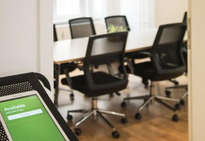 Bright meeting room seen through an open door with black mesh chairs and a wooden floor.