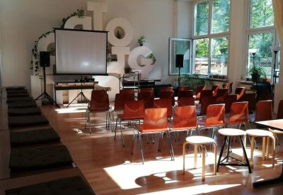 Communal presentation space with a projector screen, orange chairs, and natural light.