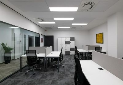 Open-plan workspace with white desks, black mesh chairs, and a glass partition wall.