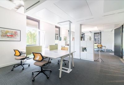 Sunlit open-plan office space with white desks, orange mesh chairs, and large windows.