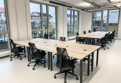 Open-plan office with long wooden desks and ergonomic black mesh chairs.