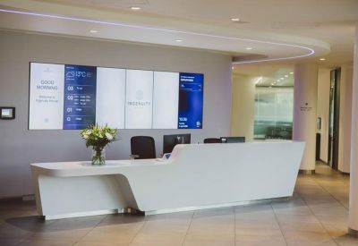 Sleek white reception desk with digital wall displays and floral arrangements.