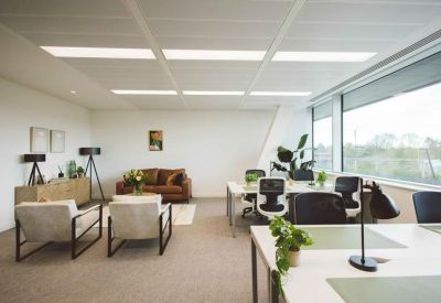 Bright breakout space with comfortable armchairs, a leather sofa, and nearby workstations.