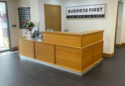 Wooden reception desk in a lobby area with corporate branding on the wall.