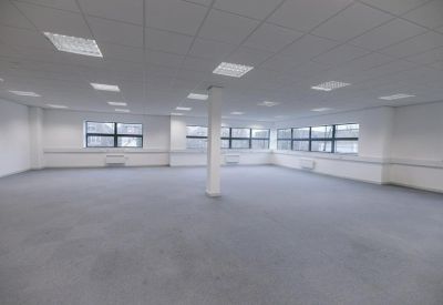 Spacious, open-plan vacant office floor with grey carpeting and white pillars.