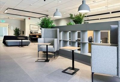 Coworking lounge area with high-backed grey armchairs and small laptop tables.