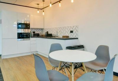 Bright breakout space with a round white table, grey designer chairs, and contemporary pendant lighting.