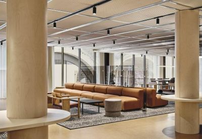 Spacious communal lounge featuring a long tan leather sofa and light wood columns.