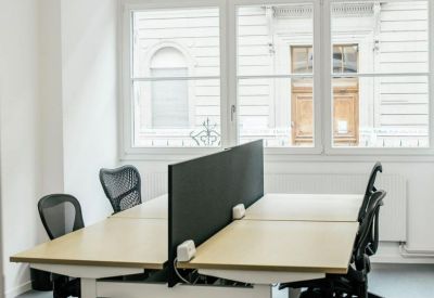 Open-plan office space with height-adjustable desks, privacy dividers, and large windows.