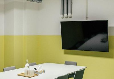 Minimalist meeting room with a white table, grey chairs, and a large wall-mounted monitor.