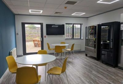 Bright communal breakroom with yellow chairs, round tables, and vending machines.