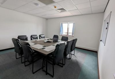 Meeting room with a large rectangular table, black leather chairs, and whiteboard.