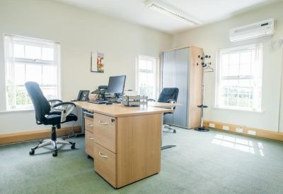 Spacious office with multiple wooden desks, ergonomic chairs, and air conditioning unit.