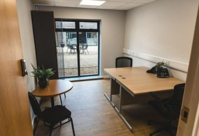 Private office featuring a large desk, a small round meeting table, and views to an outdoor courtyard.