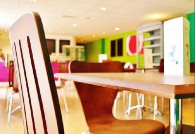 Bright communal dining area with wooden tables, modern chairs, and a colorful feature wall.