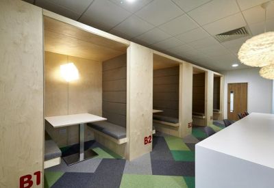 Modern breakout area with wooden acoustic pods and green geometric carpet.
