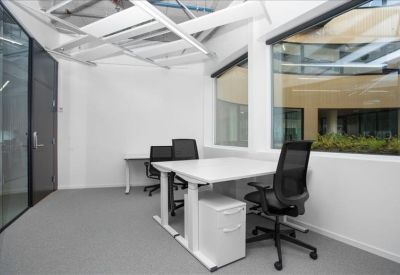 Bright private office with two sit-stand desks and a view into an internal atrium.