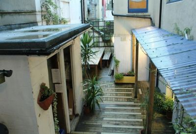 Narrow outdoor courtyard featuring wooden decking, potted tropical plants, and a corrugated plastic roof.