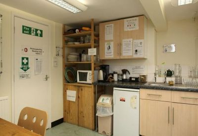 Compact communal kitchen area with light wood cabinetry, a microwave, mini-fridge, and fire safety signage.