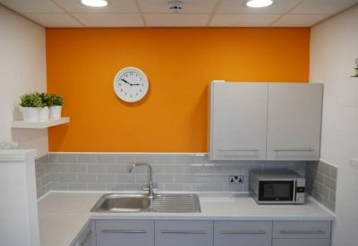 Modern communal kitchen with a bright orange feature wall, grey cabinetry, and subway tile backsplash.
