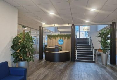 Modern reception lobby with curved desk, wood-style flooring, and indoor plants.
