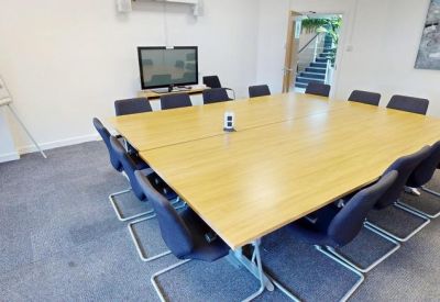 Large square meeting table with blue chairs and a wall-mounted screen.