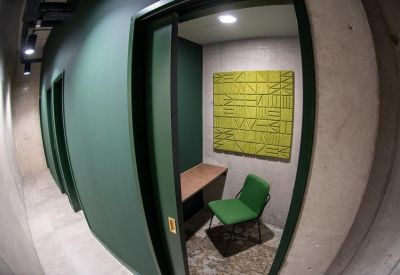 Small green-walled private phone booth or single-person workspace with a desk and chair.