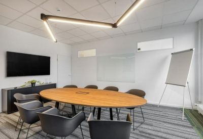 Spacious boardroom with a large oval wooden table, black chairs, and a wall-mounted screen.