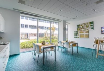Modern communal kitchen and dining area with teal flooring and bright window views.