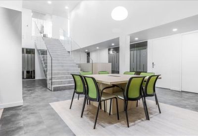 Communal area with a square wooden table, green chairs, and a modern open staircase.