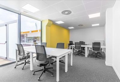 Modern open-plan office space featuring white desks, mesh chairs, and a bright yellow accent wall.