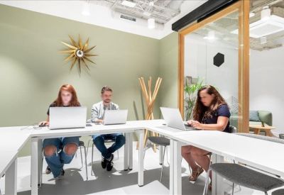Co-working space with long wooden tables, industrial ceiling pipes, and framed wall art.