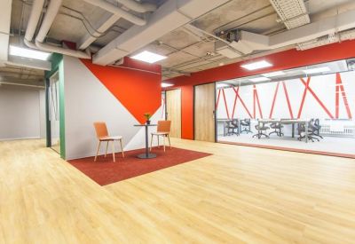 Small meeting area with two orange chairs and a round table in front of a glass wall.