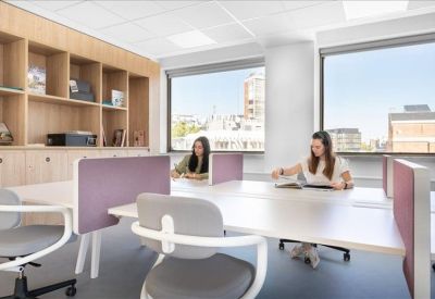 Bright open-plan office with desks facing large windows and city views.