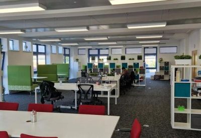 Modern coworking space with green privacy booths, white desks, and red chairs.