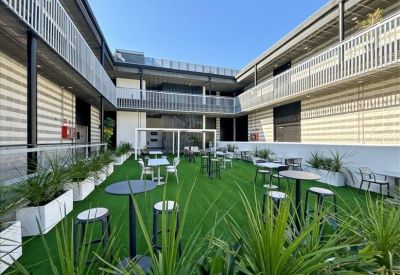 Spacious internal courtyard with artificial turf, white cafe tables, and potted plants.