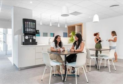 Communal kitchen and breakout area with a coffee machine, white cabinetry, and dining tables.